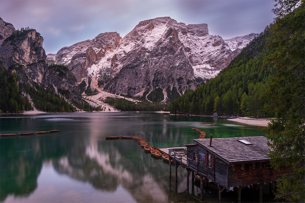 Sunset reflected at Lake Braies with wooden boats and snow-dusted peaks in the Dolomites