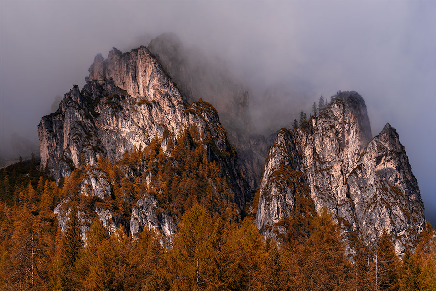 Misty cliffs above fall-colored trees near Lake Landro in the Dolomites