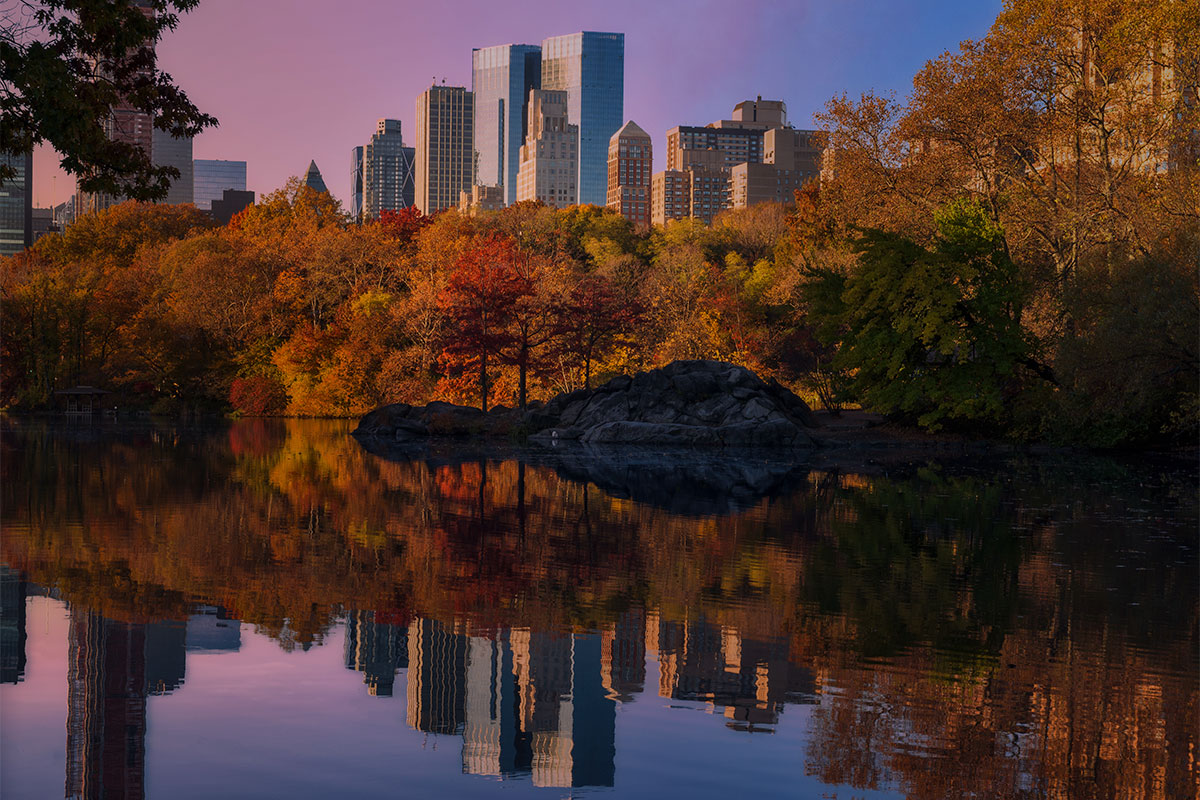 Central Park in autumn with the New York City skyline reflected in calm water during early morning light
