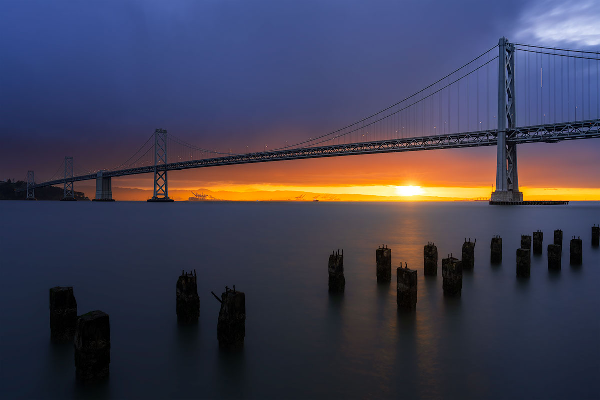 San Francisco–Oakland Bay Bridge at sunset with long exposure water and glowing horizon