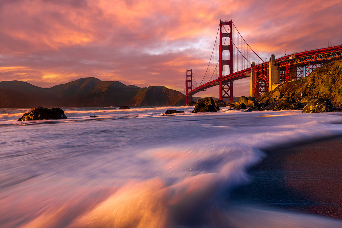 Golden Gate Bridge photographed from the shoreline at sunset with long-exposure waves, San Francisco
